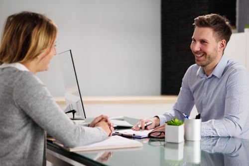 One-to-one workplace needs assessment conversation between an assessor and an employee in a professional setting.